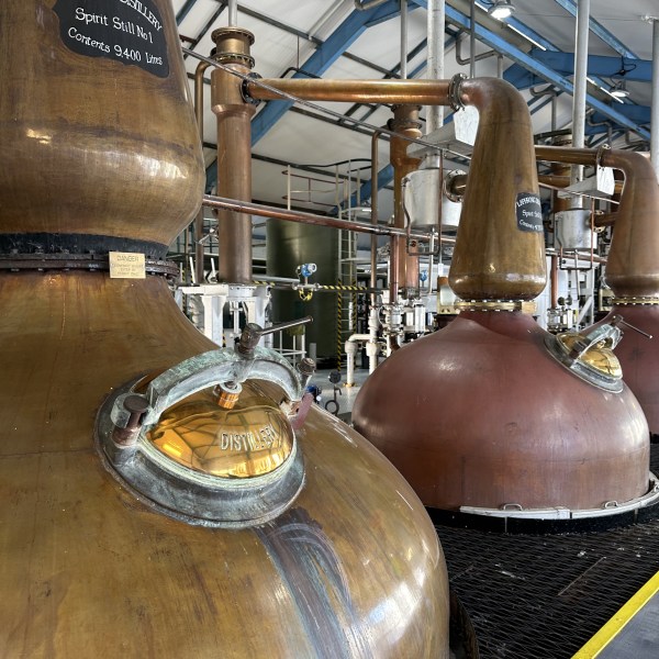 Copper distillery stills inside a distillery with labels and pipes.