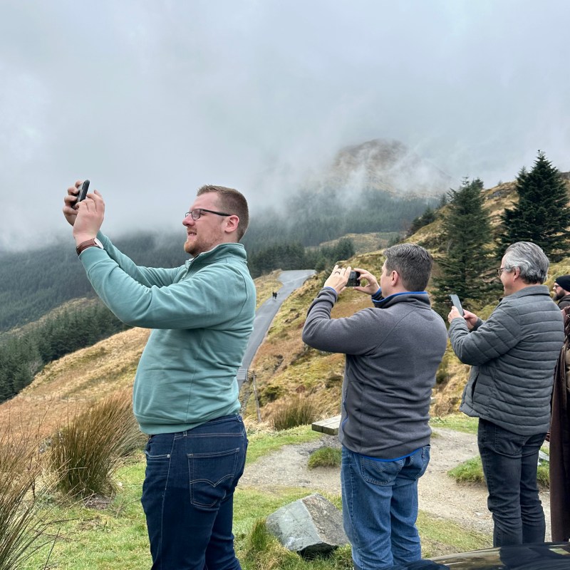 Four people taking photos of a foggy mountain landscape with their phones.