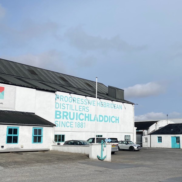 White distillery building with 'Bruichladdich' logo and parked cars on a sunny day.