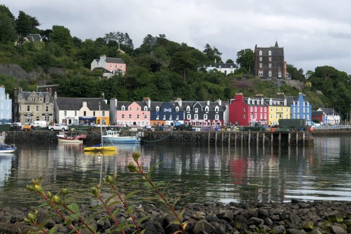 Colorful houses by a waterfront with a hill and cloudy sky.