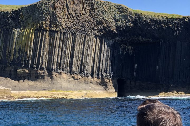 Person on boat looking at cliff with basalt columns.