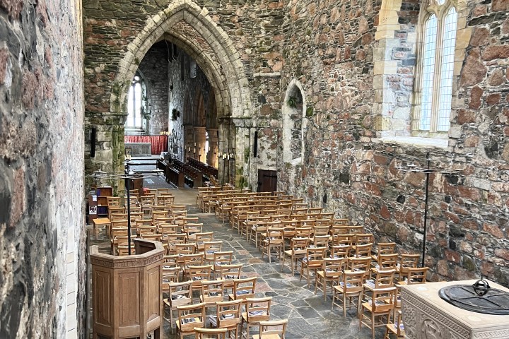 Stone church interior with wooden chairs, arched ceiling, and a carved stone font.