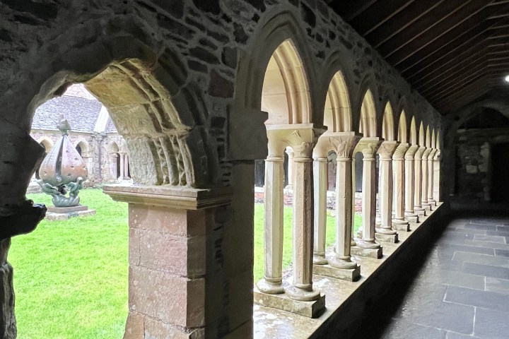 Stone archway with columns, view of courtyard and grass outside.