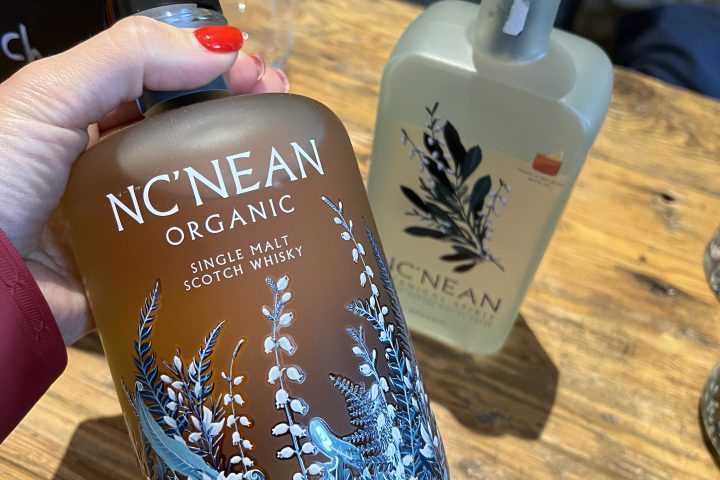 Hand holding bottle of Nc'nean Organic Scotch Whisky with decorative label.