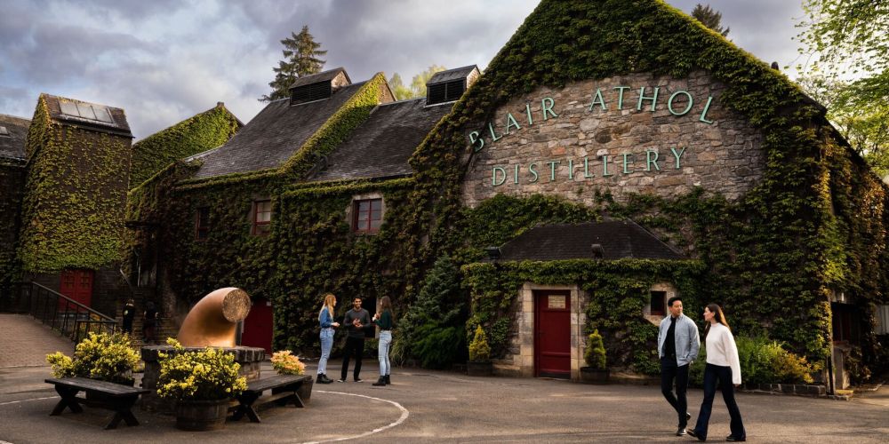 Stone building with Blair Athol Distillery sign, ivy-covered walls, and people walking.