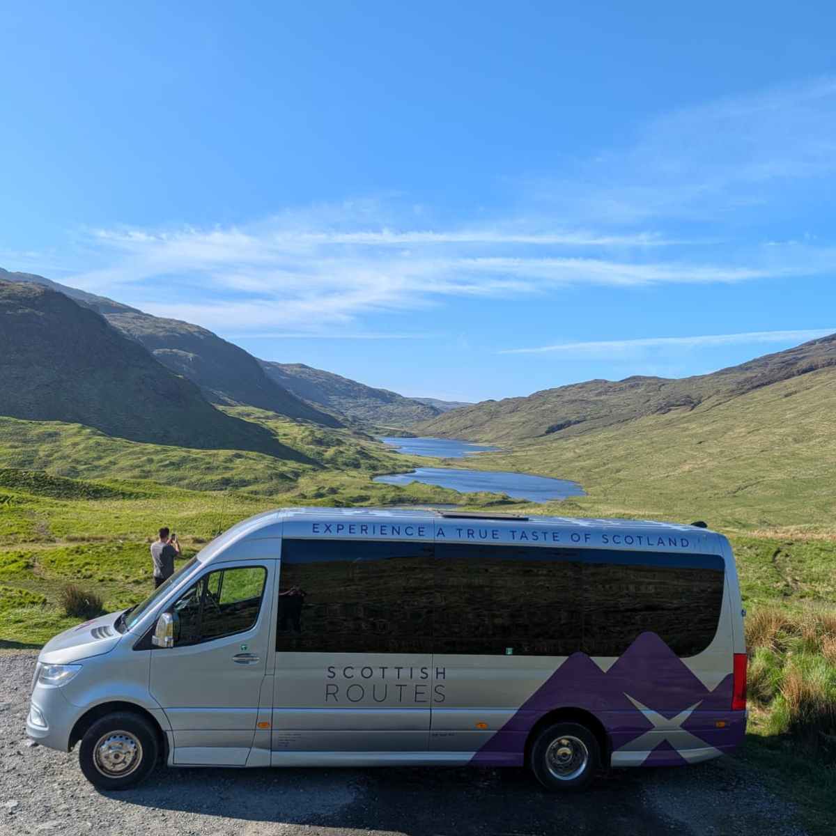 Tour van parked on a scenic hill with mountains and blue sky.